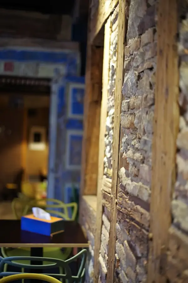Holzpfosten vor einer Wand aus Naturstein, dahinter bunte Stühle