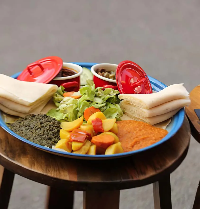 Große Platte mit Injera, Salat, Linsen, Gemüse und kleinen roten Emaille-Töpfen