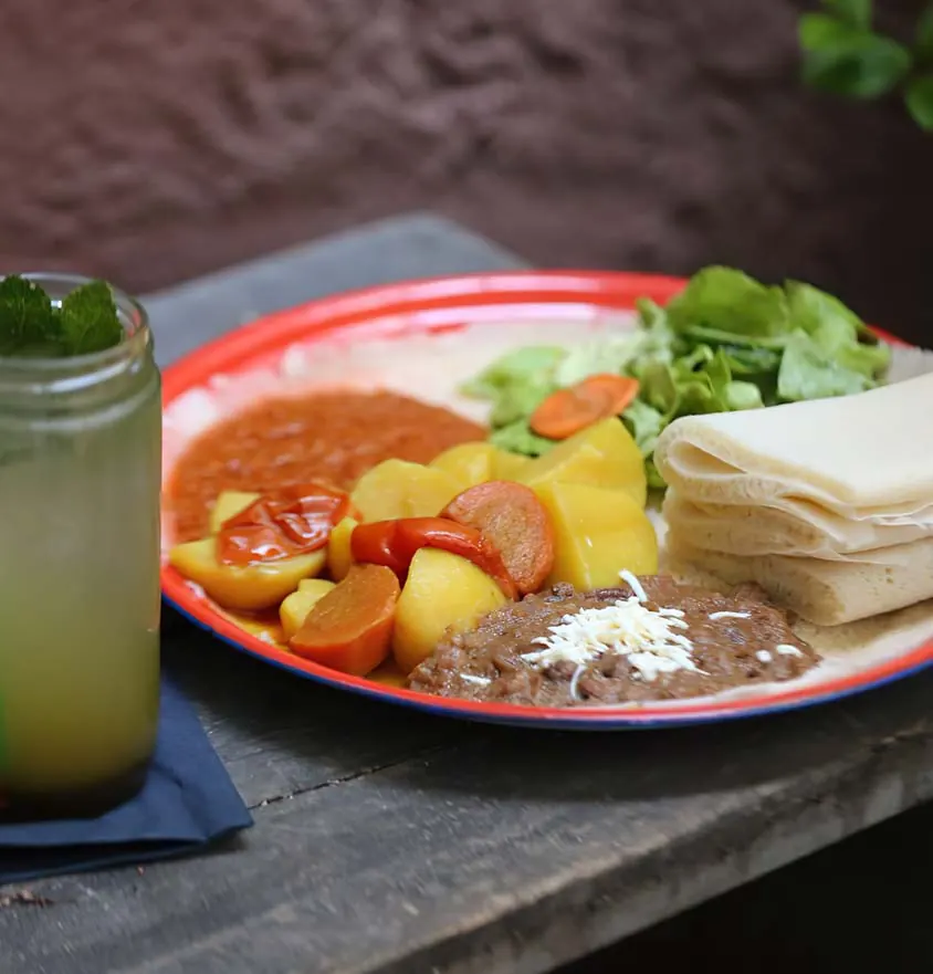 Teller mit Kartoffeln, Karotten, Linsen, Salat und Injera, daneben eine grüne Limonade