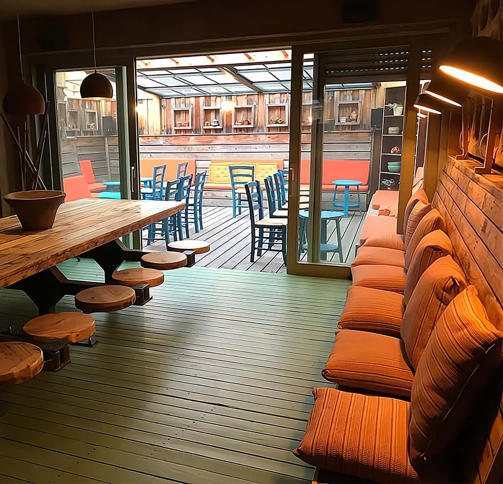 Langer Holztisch mit Baumstumpf-Hockern, dahinter die überdachte Terrasse