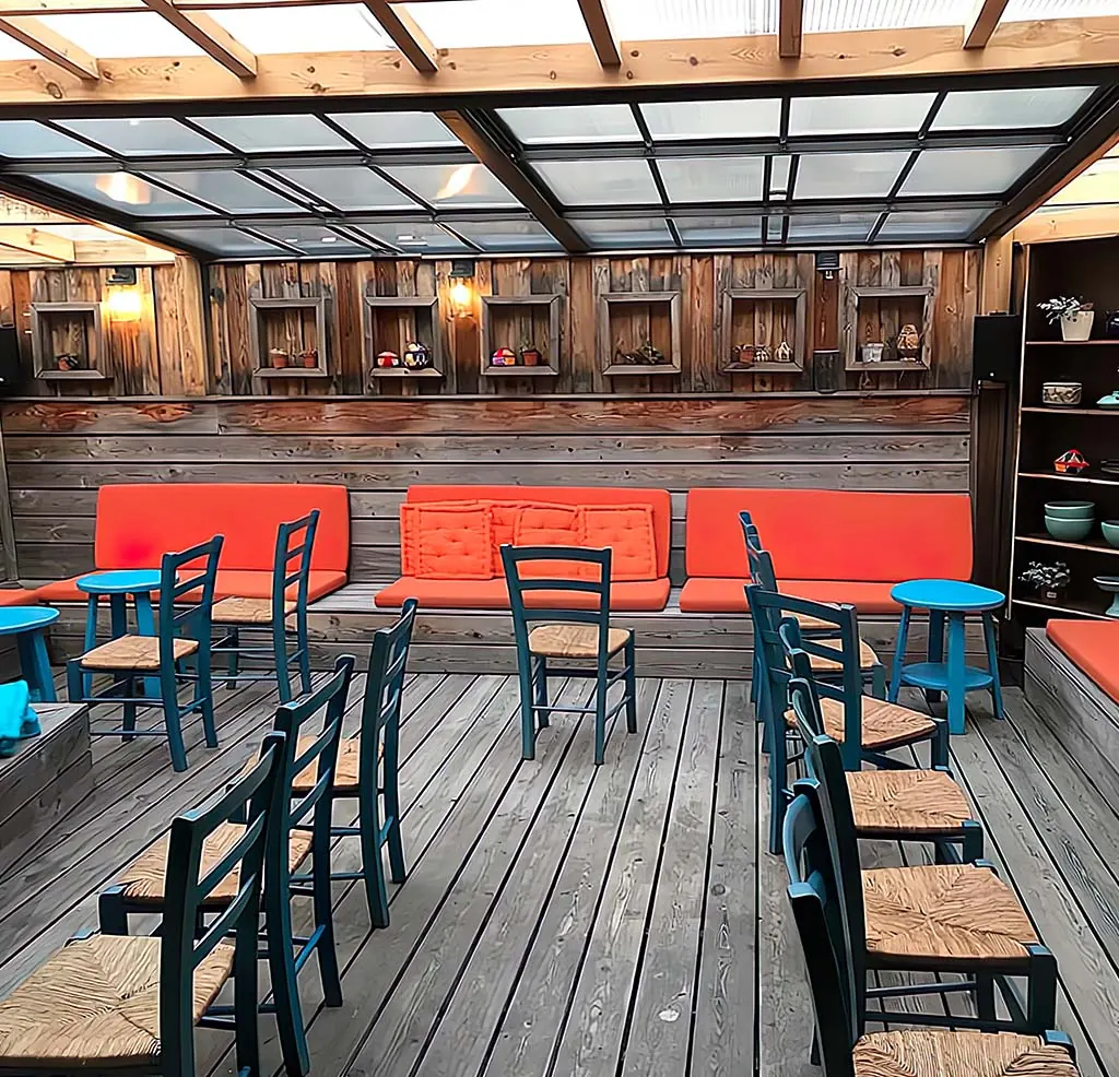 Überdachte Terrasse mit Holzdielen, orangen Sitzpolstern und blauen Stühlen